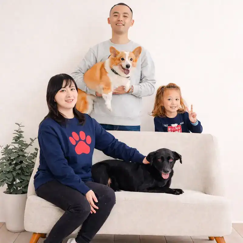 Dalia, recovered and glossy coated, sitting on a sofa with her adoptive family and their corgi